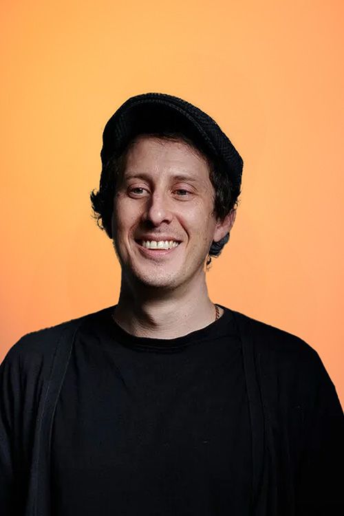 A man wearing a hat and a black shirt smiles for the camera