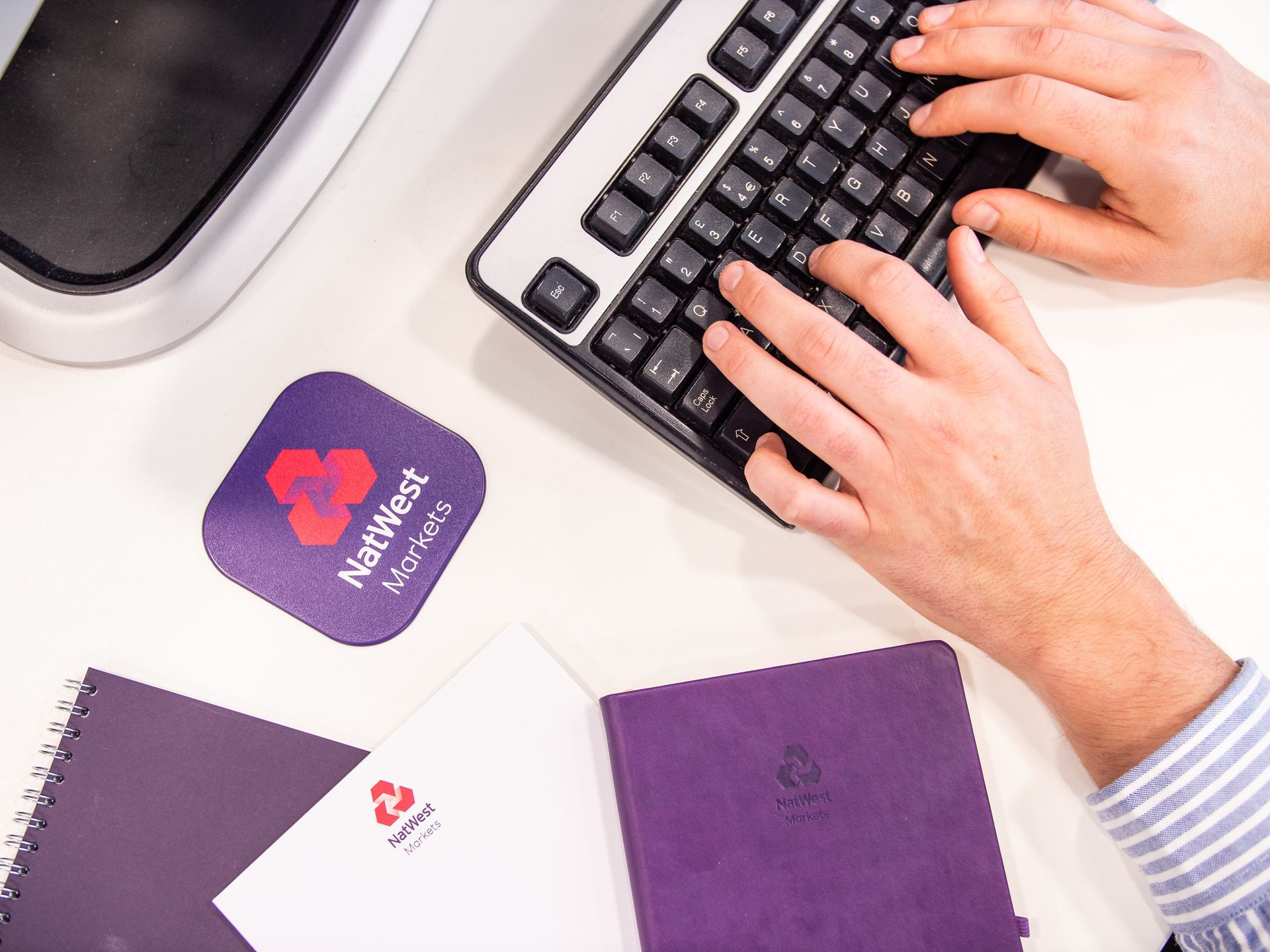 A person is typing on a keyboard next to a purple notebook