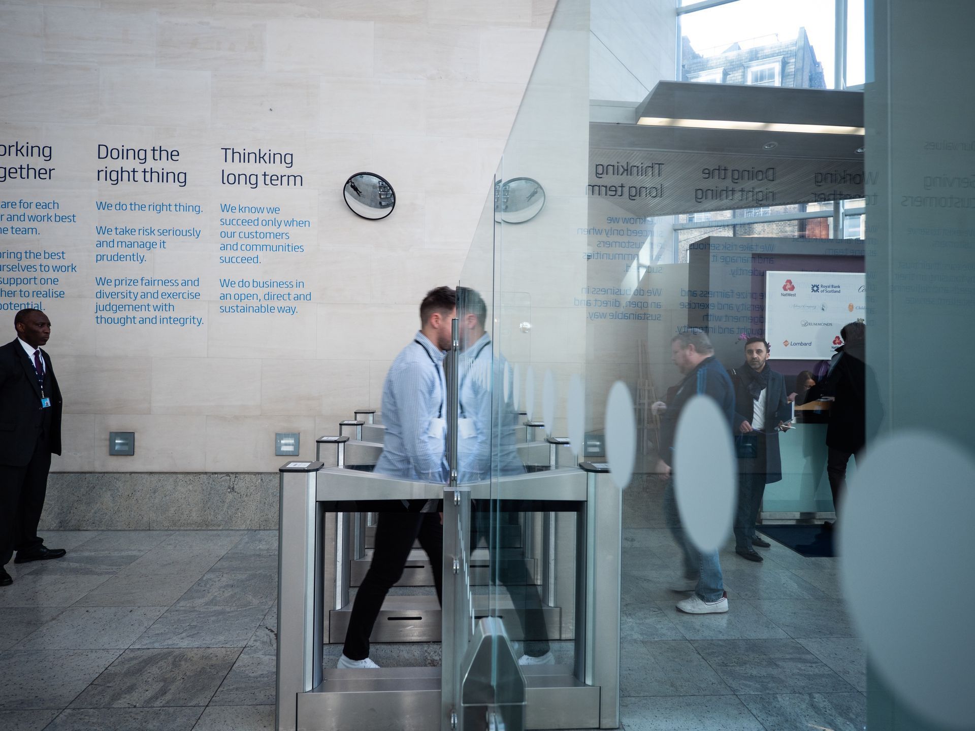 A man in a blue shirt is walking through a glass door