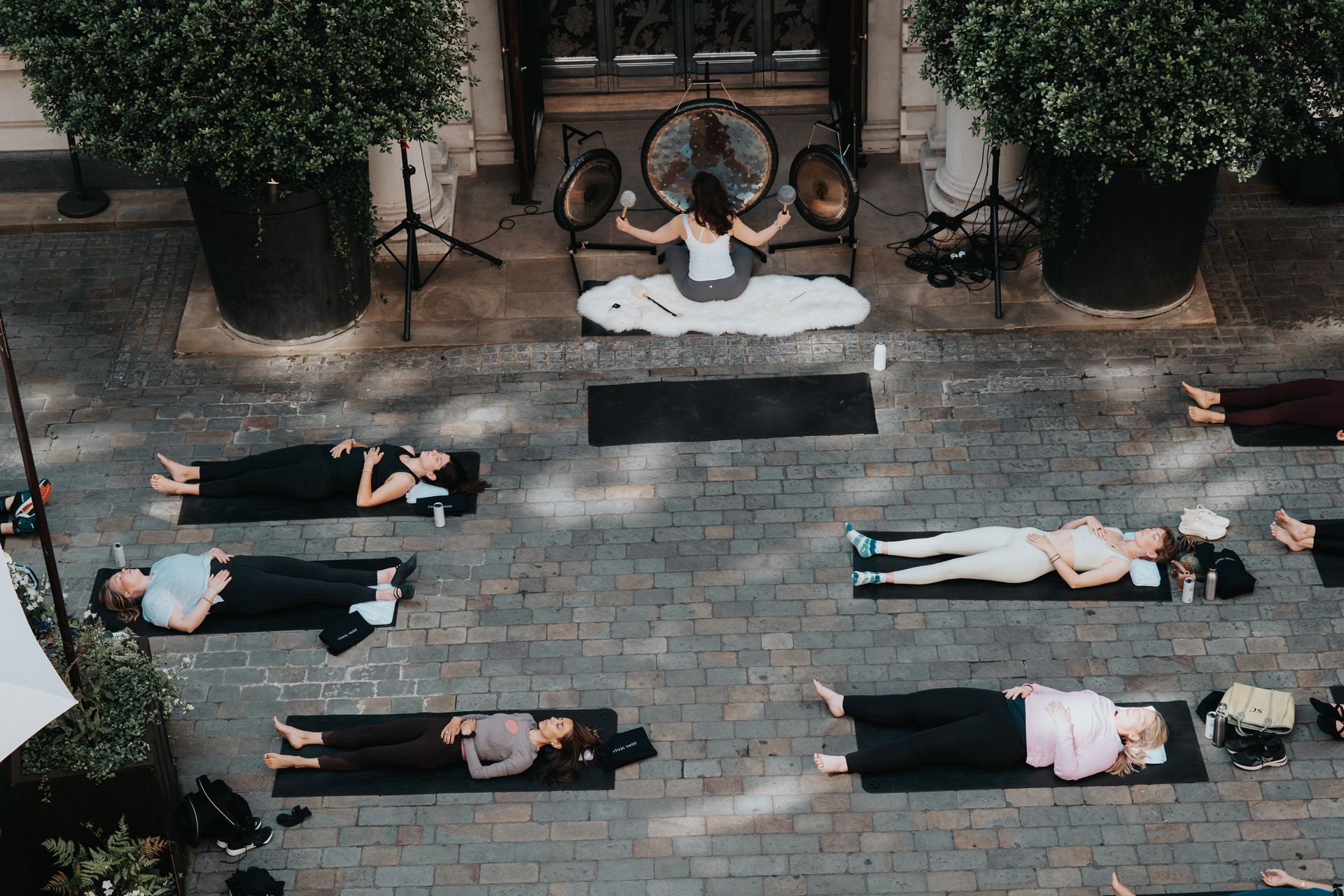 A group of people are laying on yoga mats on a brick sidewalk.