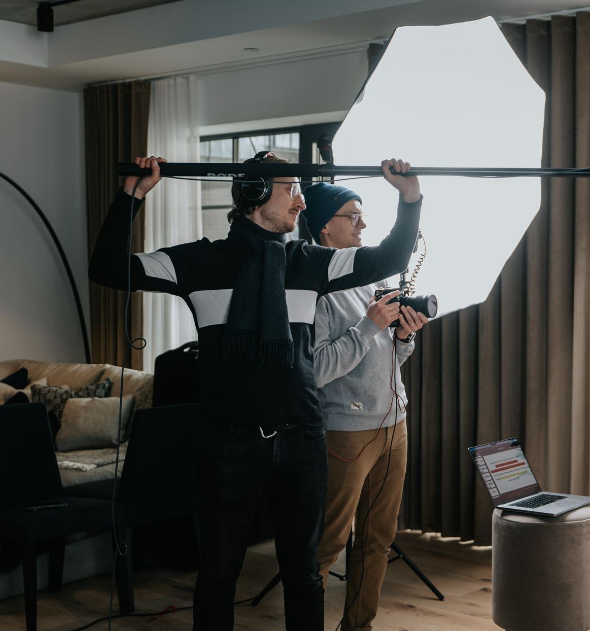 two men are standing in a living room holding umbrellas and cameras .