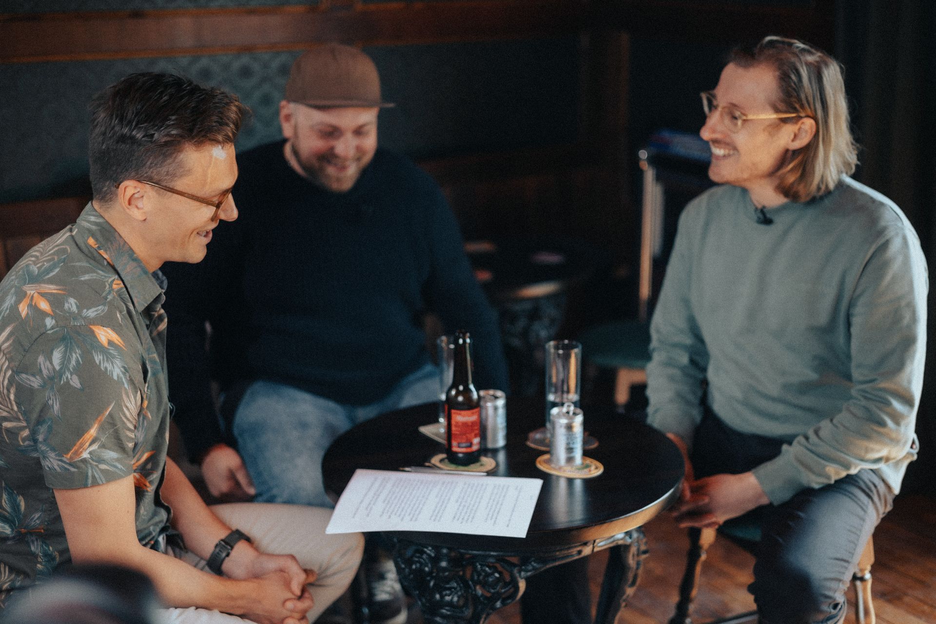 Three men are sitting at a table with a bottle of beer on it.