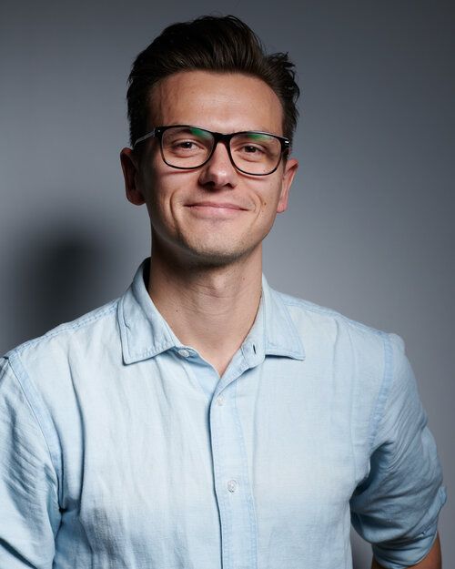 A man wearing glasses and a light blue shirt is smiling for the camera.