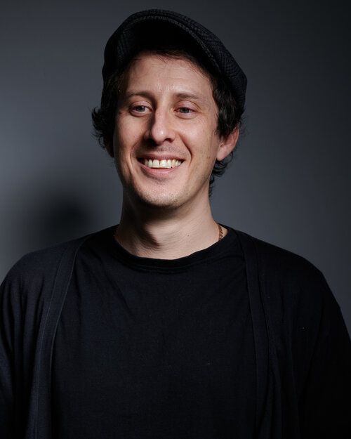 A man wearing a hat and a black shirt smiles for the camera