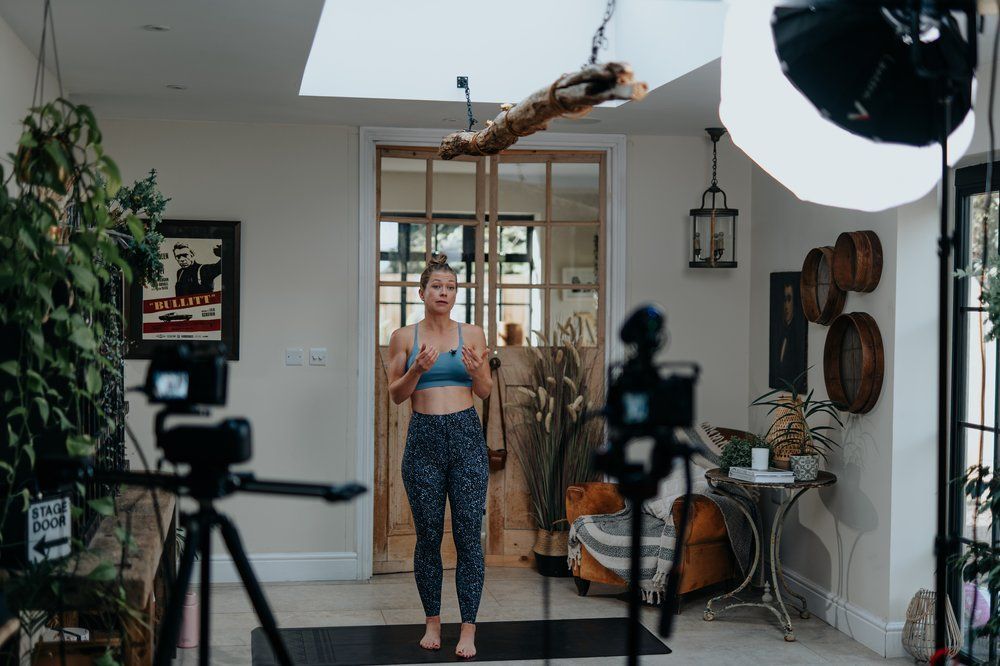 A woman is standing on a yoga mat in front of a camera.