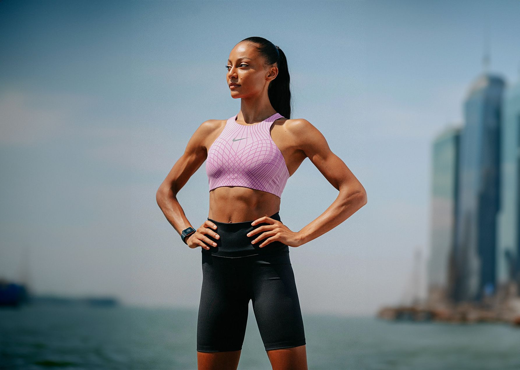 A woman is standing with her hands on her hips in front of a body of water.