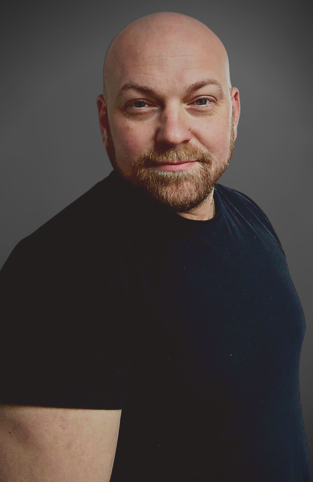 A bald man with a beard is wearing a black shirt and looking at the camera.