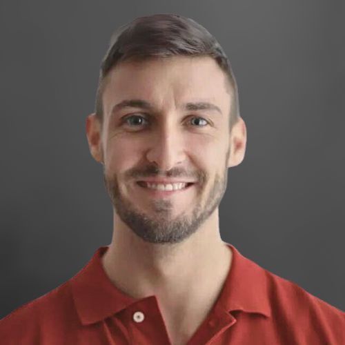 A man with a beard is wearing a red polo shirt and smiling.