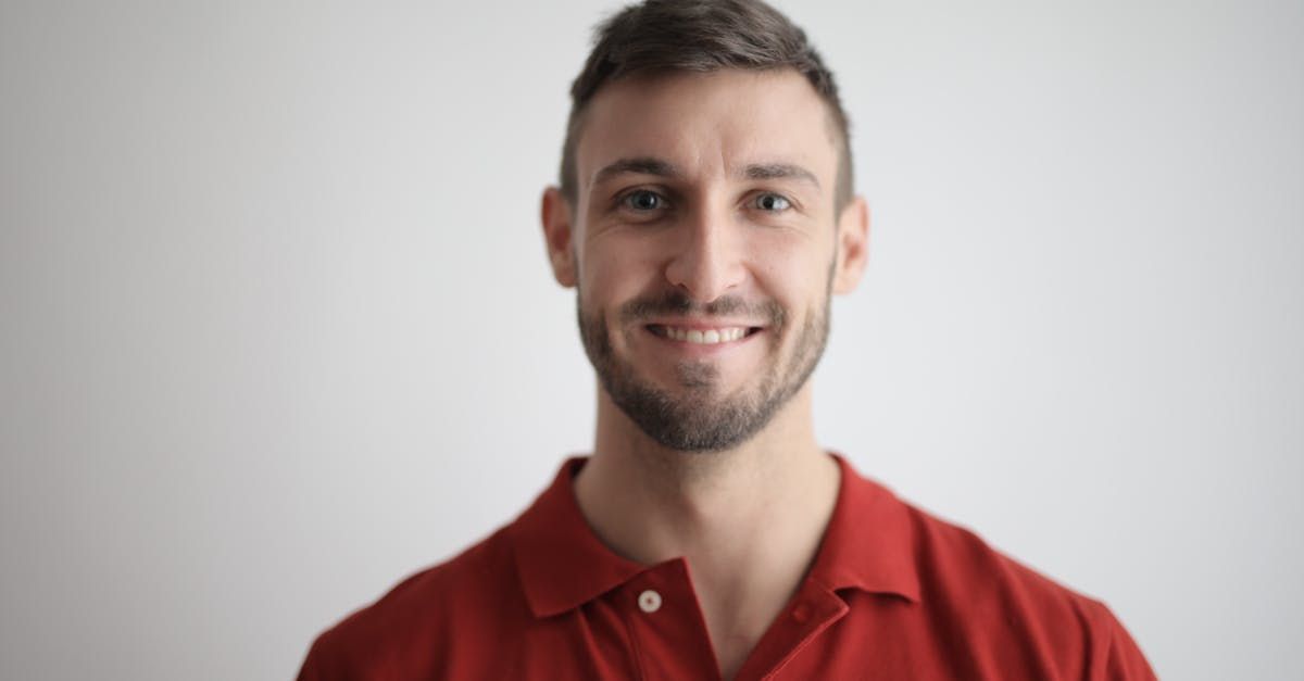 A man with a beard is wearing a red polo shirt and smiling.