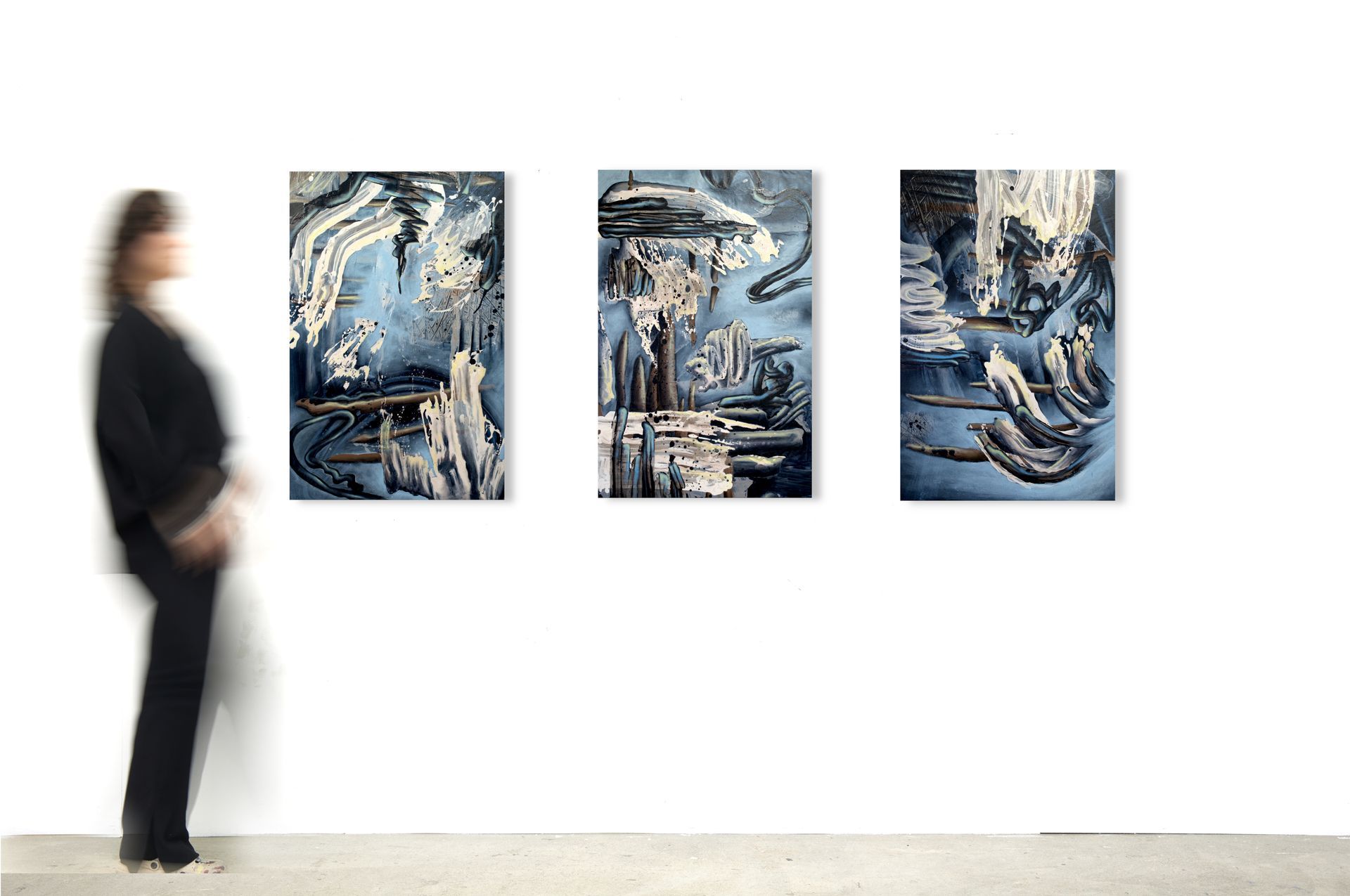 Triptych of blue abstract paintings with splashes and artist walking by, by Lala Drona