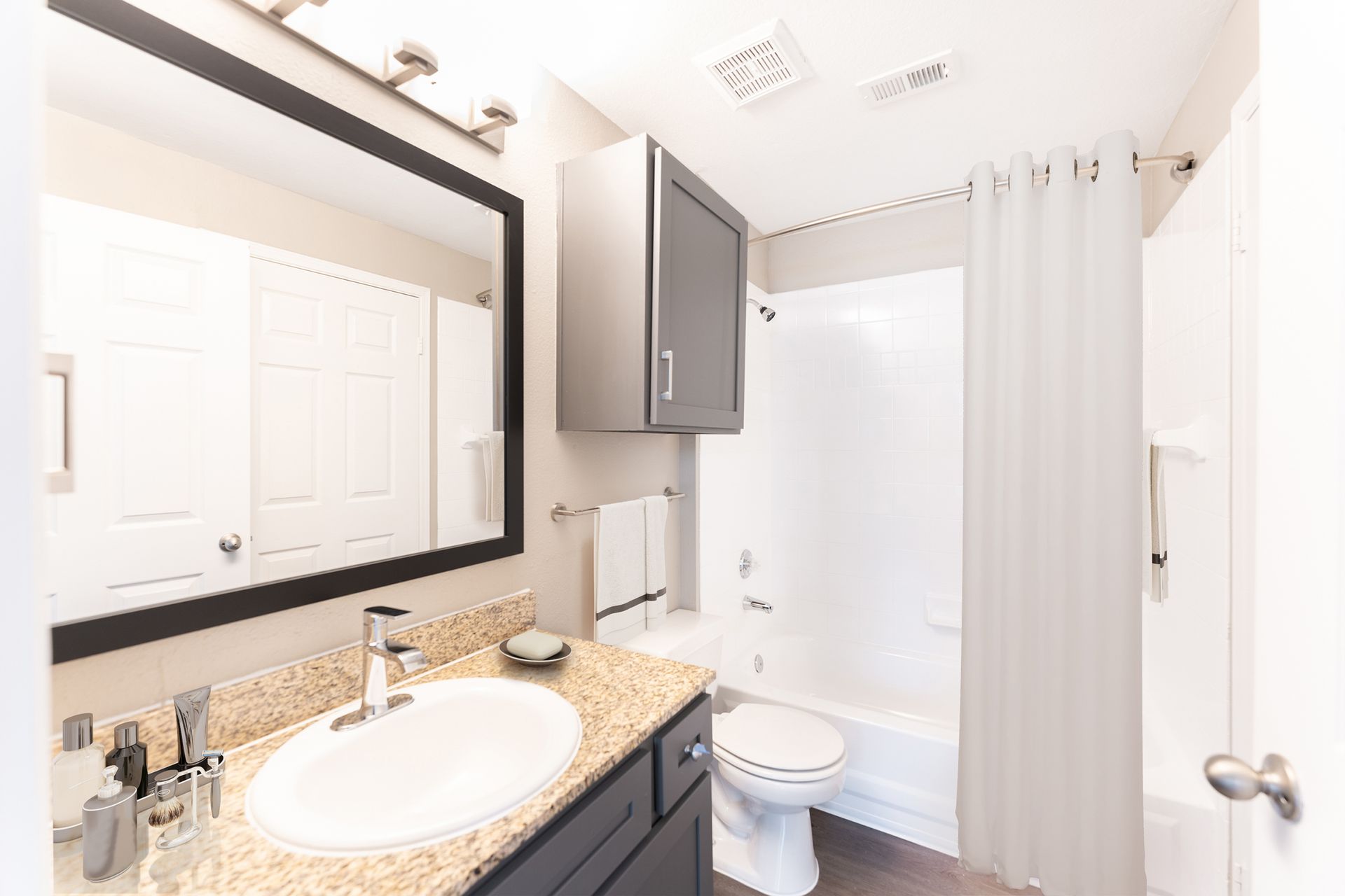 A bathroom with a sink, toilet, bathtub and mirror at Marquis Champions Forest offers apartments for rent in Houston, TX.