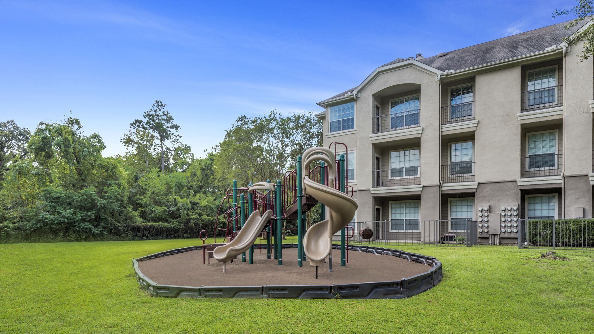 A playground with a slide and a slide in front of apartment buildings at Marquis Champions Forest offers apartments for rent in Northwest Houston, TX.