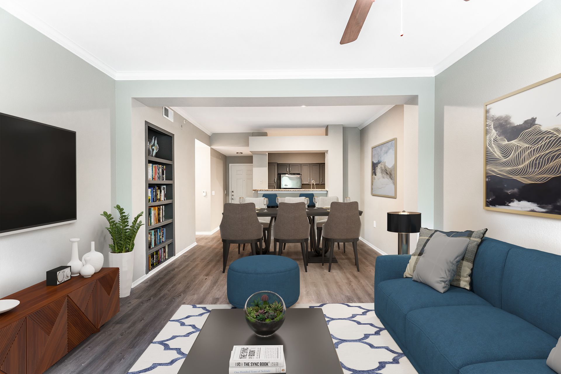 A living room with a blue couch overseeing the kitchen at Marquis Champions Forest offers Houston apartments for rent.