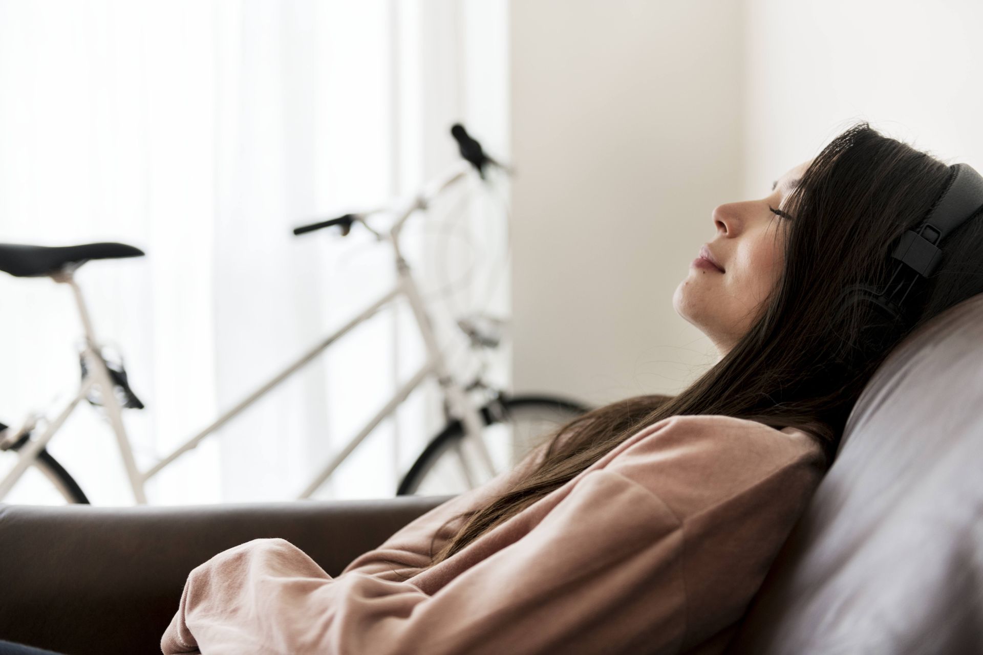 A women laying on her sofa with a headphone and next to a white bike.
