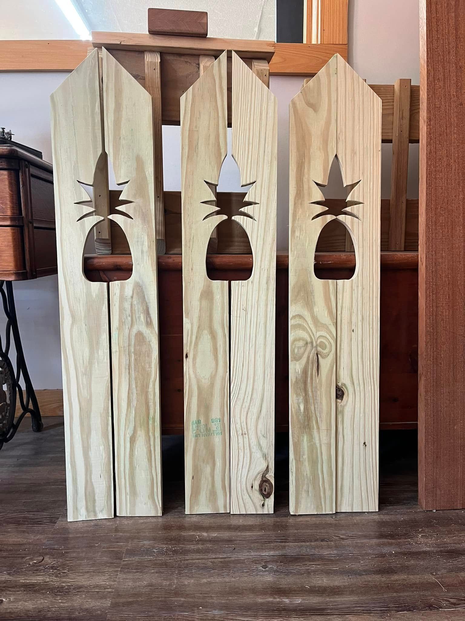 A wooden fence with pineapples cut out of it is sitting on a wooden floor.