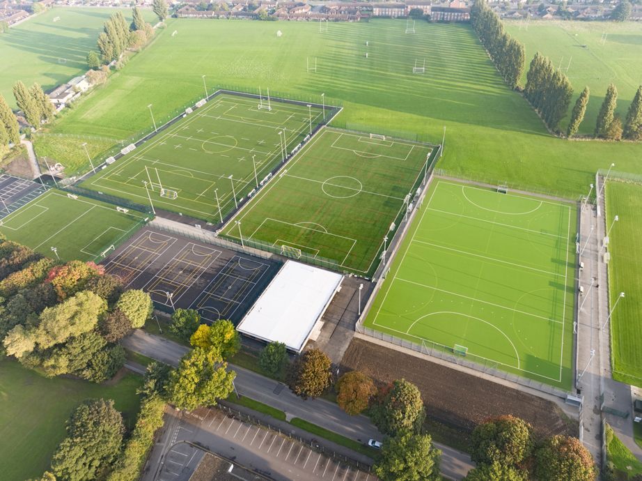 Aerial view of a sports complex with multiple green playing fields and a white covered structure.