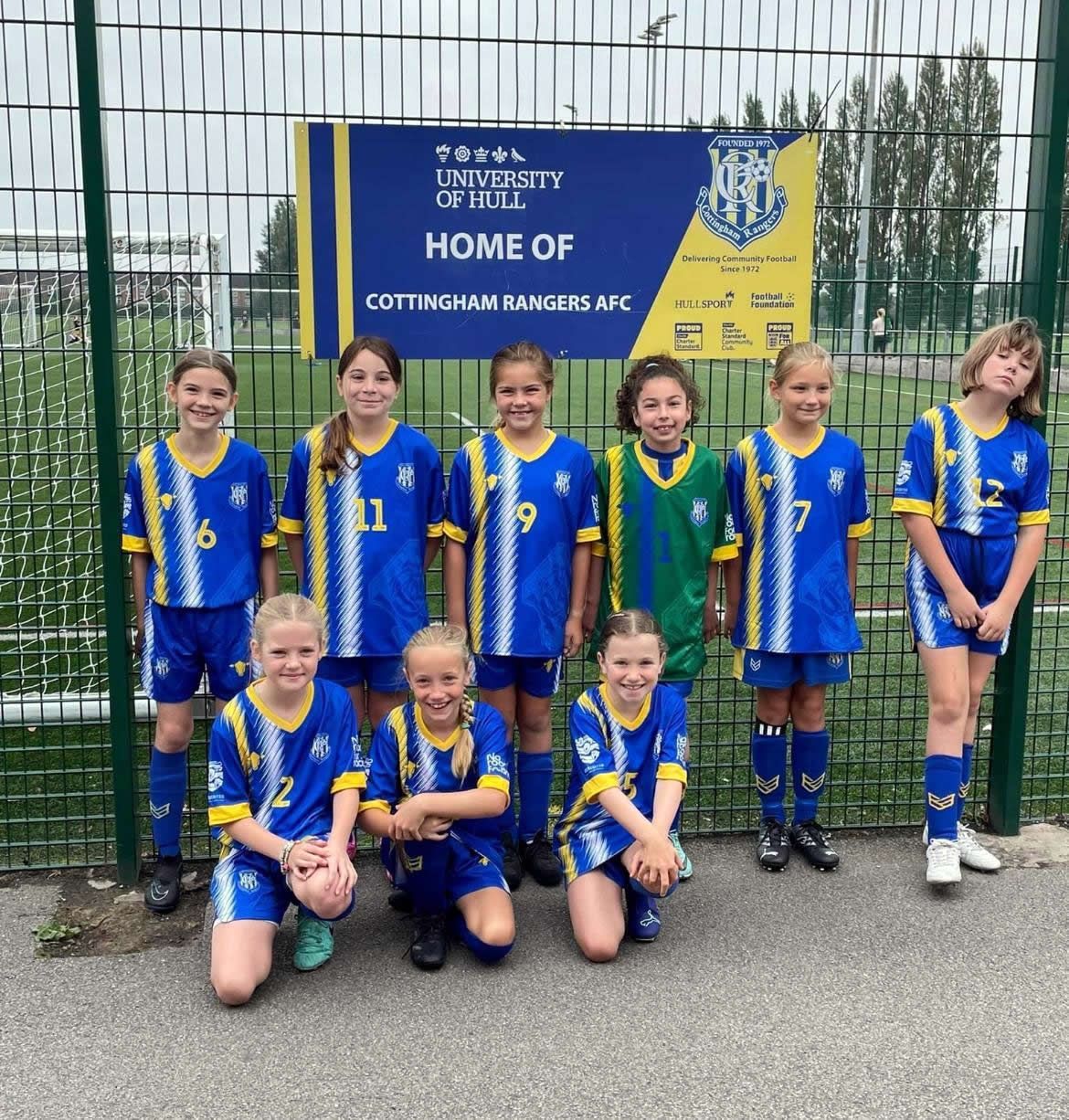 Youth soccer team in blue and yellow uniforms posing in front of a sign at the University of Hull.
