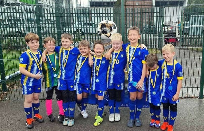 Youth soccer team in blue and yellow uniforms, posing with medals.