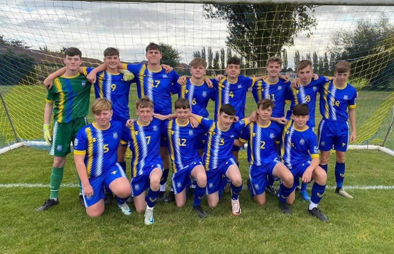 Soccer team posing in blue and yellow uniforms in front of a goal net.