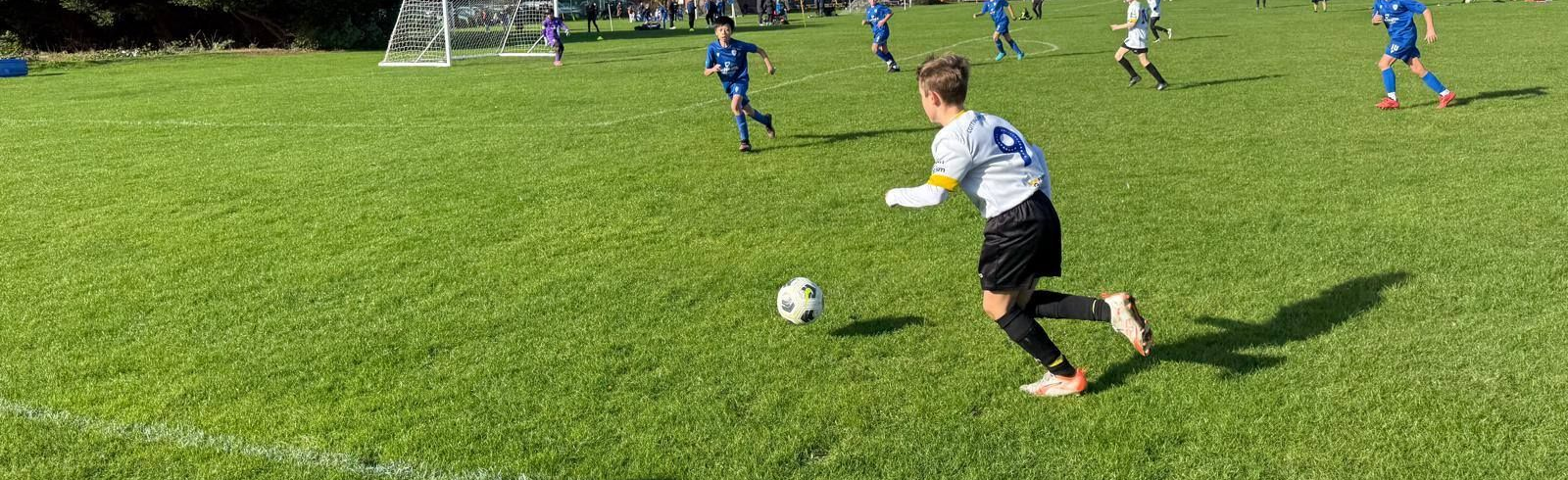 Bald man in black jacket smiles, standing on a grassy field with houses and trees in the background.