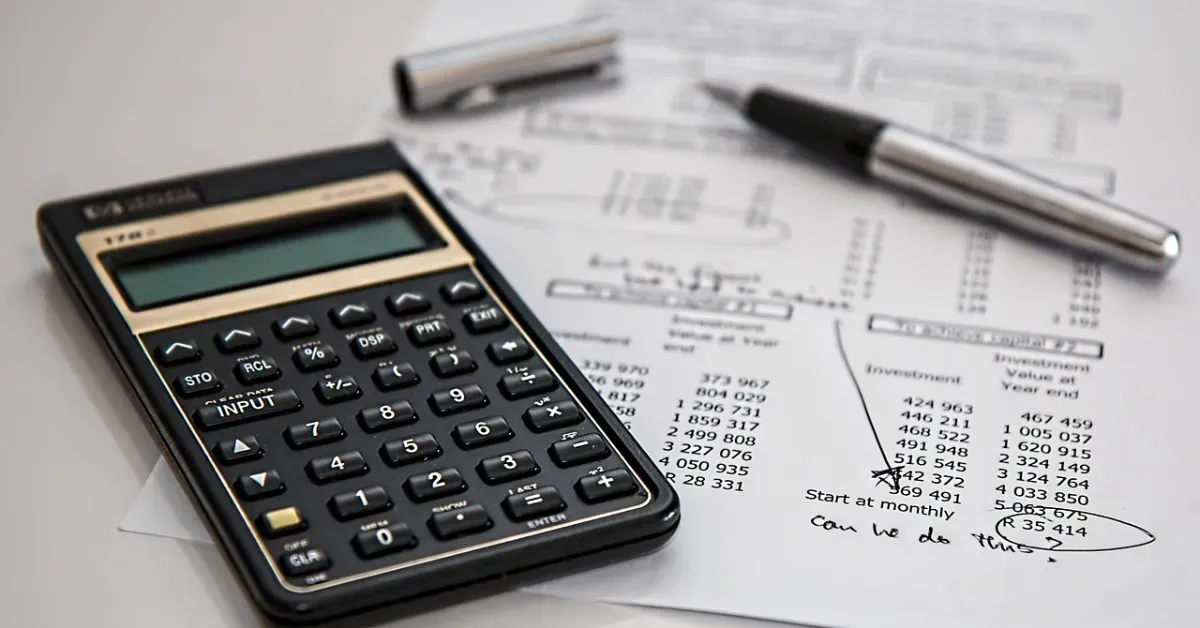 Calculator beside pen and paper with printed financial calculations on a desk