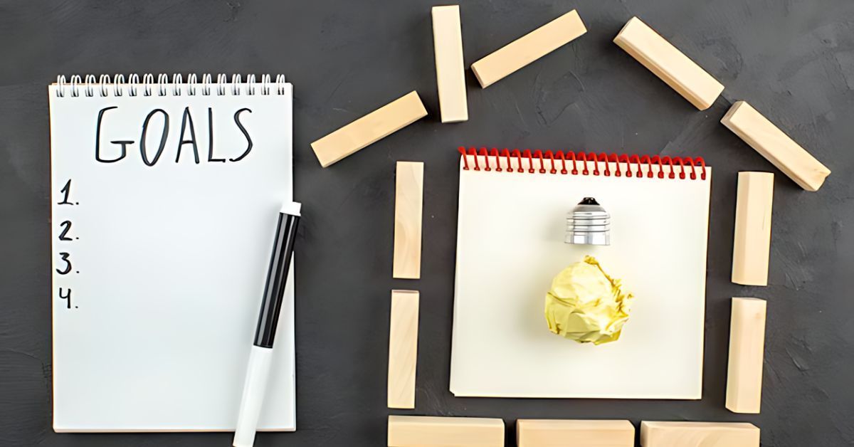 Goals list with four numbered lines beside a lightbulb inside a house shape made of wooden blocks.