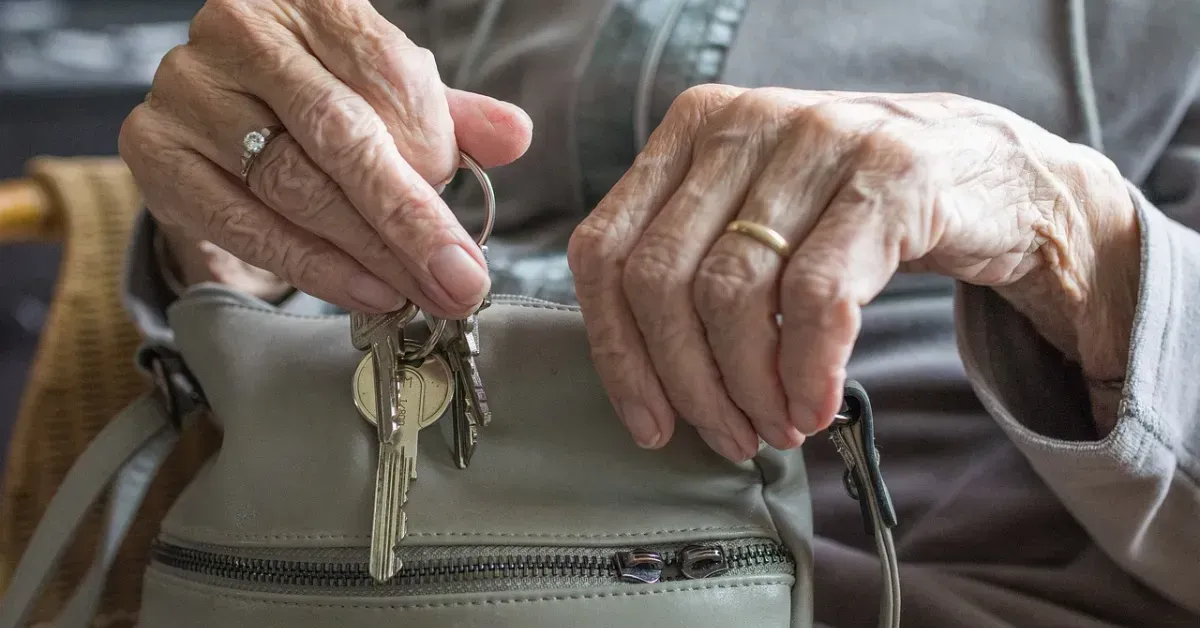 Hands holding keys over a beige handbag, with an elderly person's hands visible in the background.