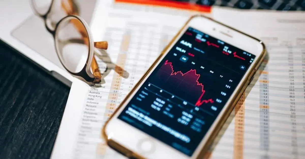 Smartphone displaying a red stock chart beside eyeglasses on financial papers