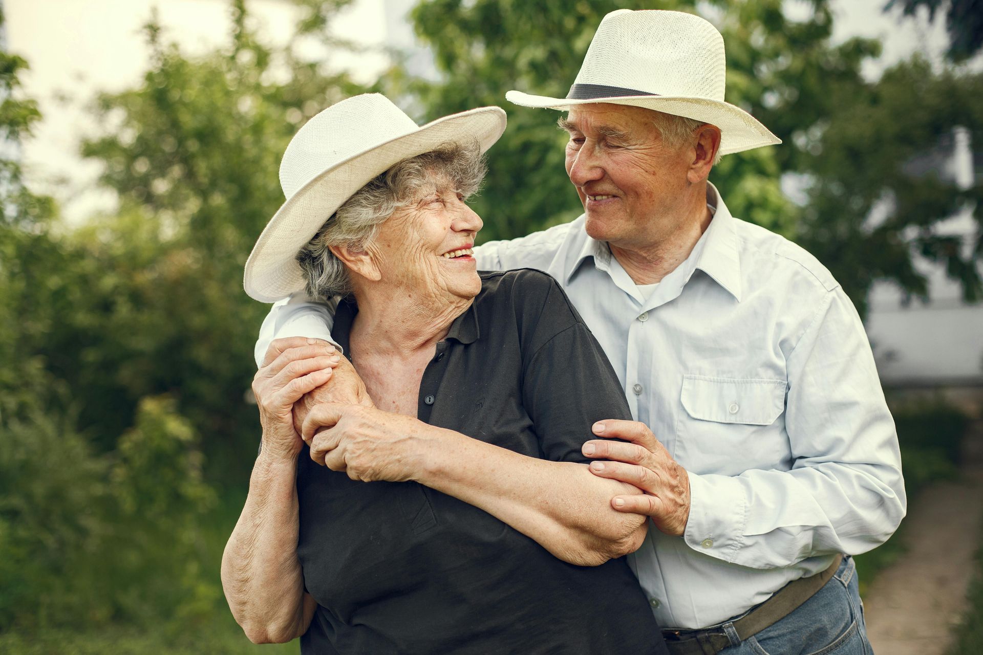 Two people in white hats smiling and embracing outdoors in a green field