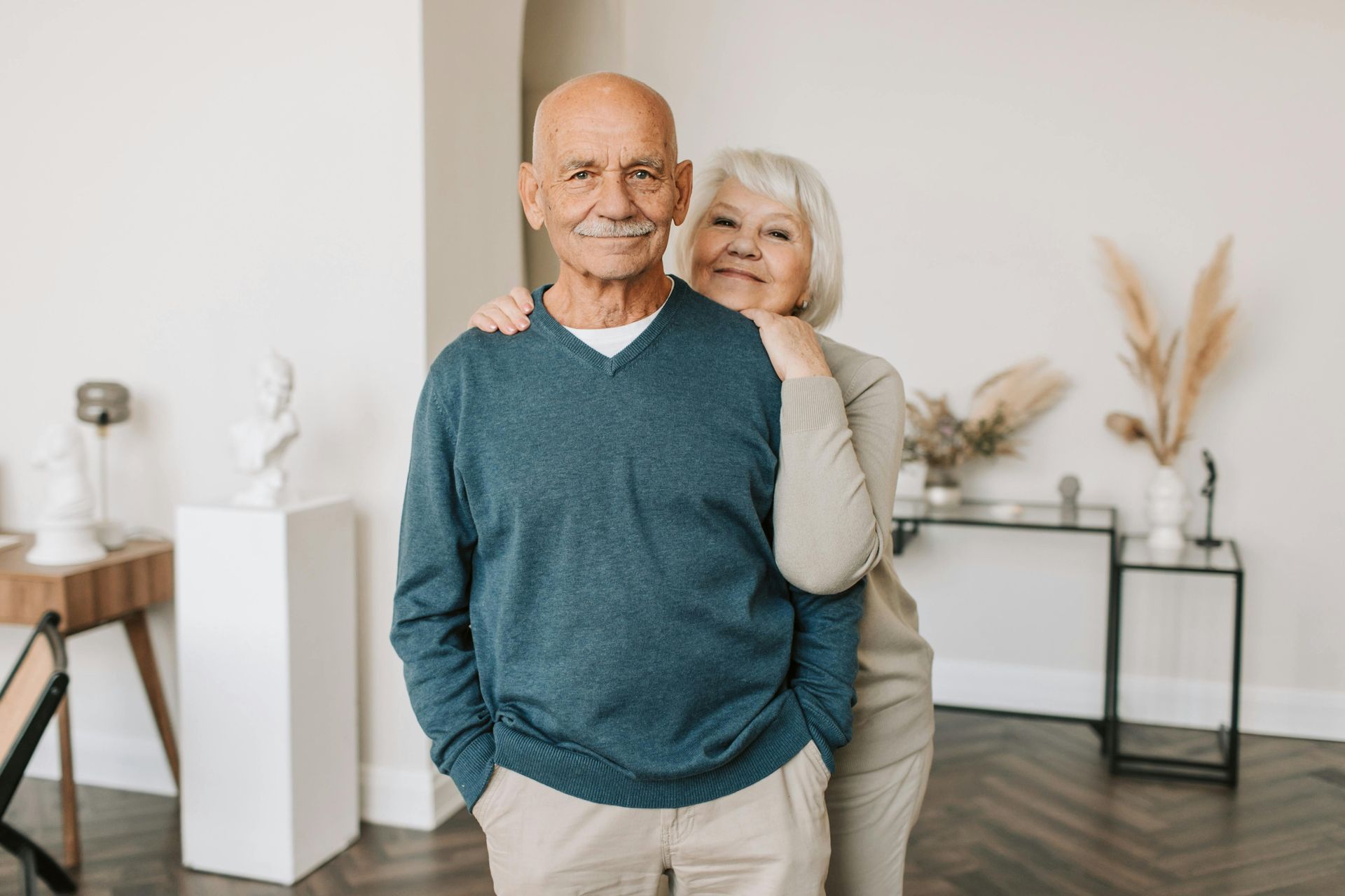 Smiling couple posing in a bright living room, with one standing behind the other.