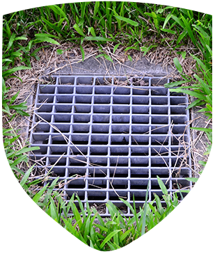 A metal grate is sitting in the grass next to a drain.