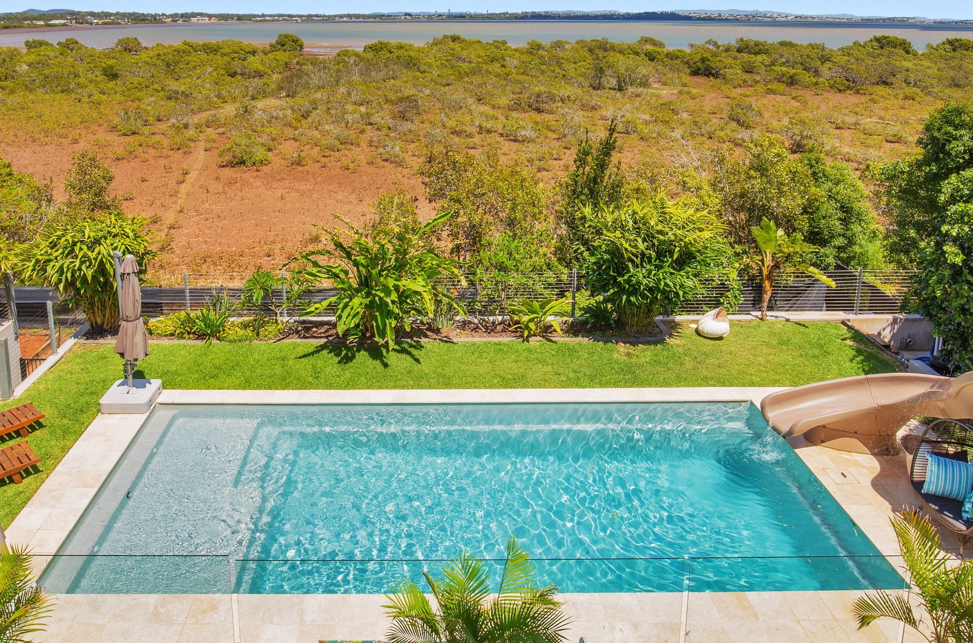 Rectangular swimming pool in backyard, green grass, trees, and marsh in the background.