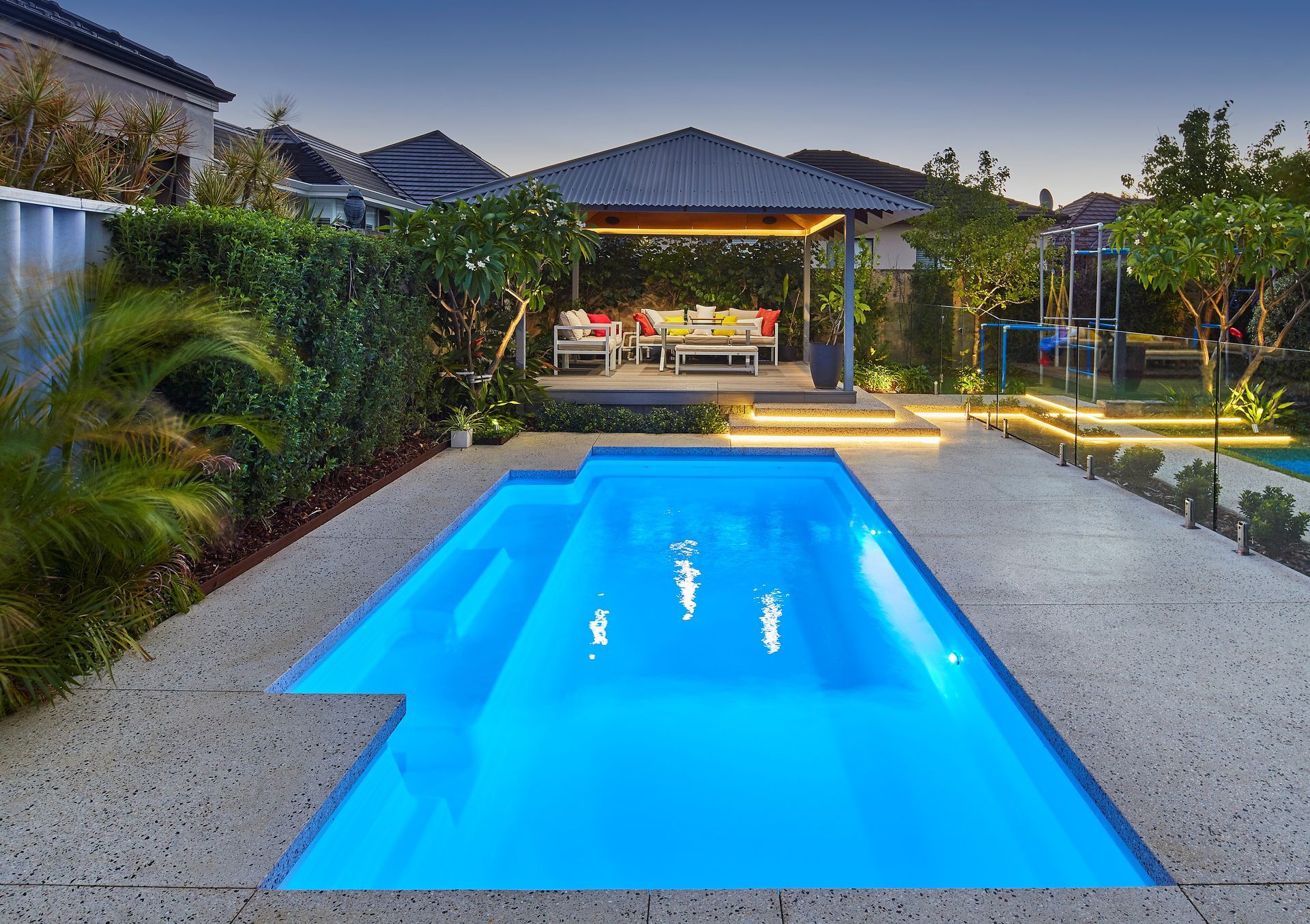 Pool with blue water, outdoor gazebo with seating, and landscaping at dusk.
