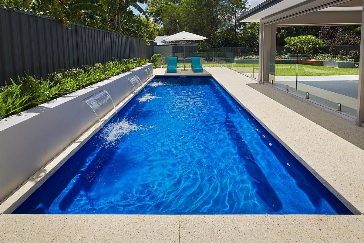 Long, rectangular blue swimming pool with water feature and lounge chairs.