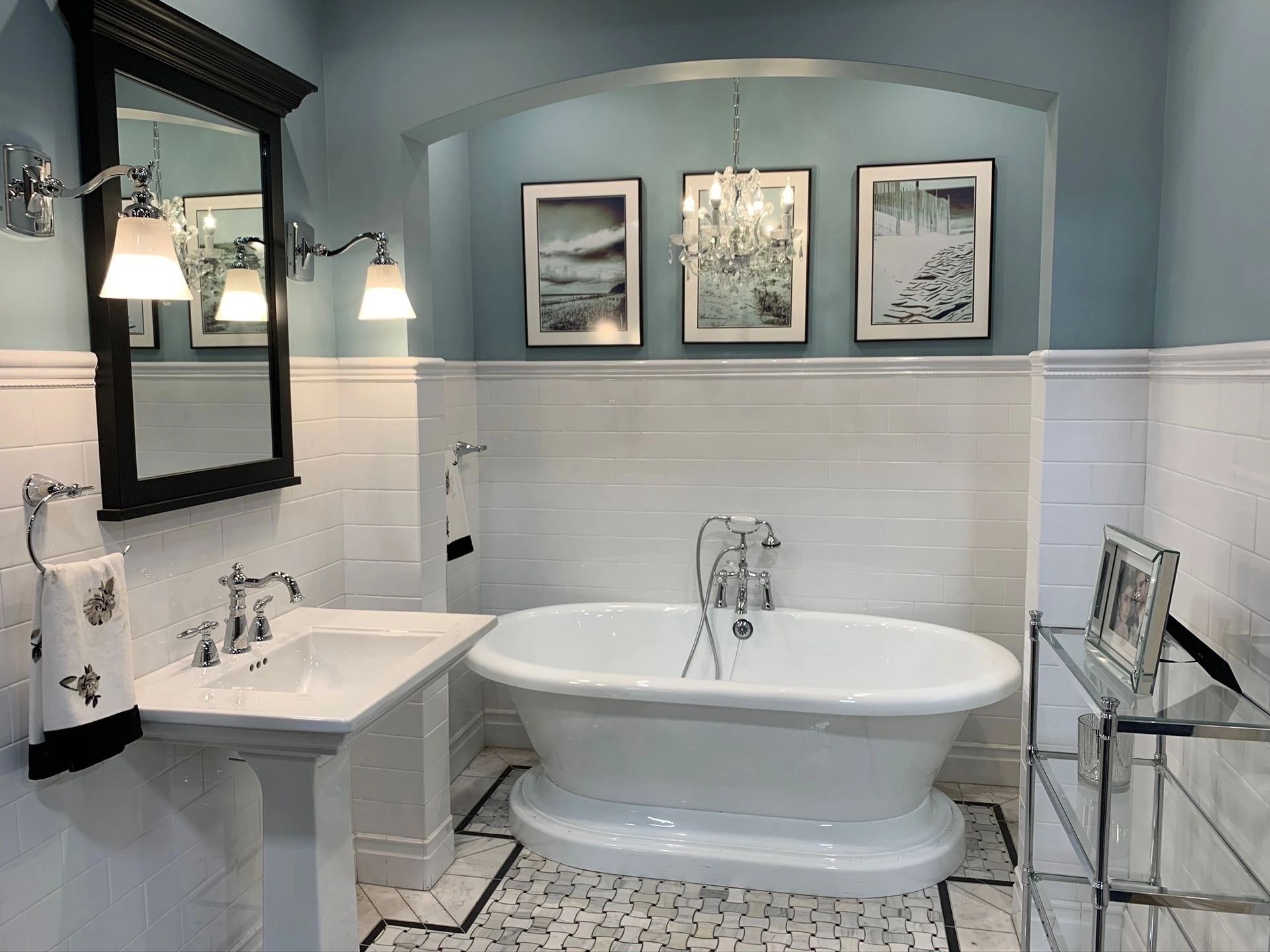 Bright blue and white bathroom with clawfoot tub, vanity, mirror, and framed art above wainscoting