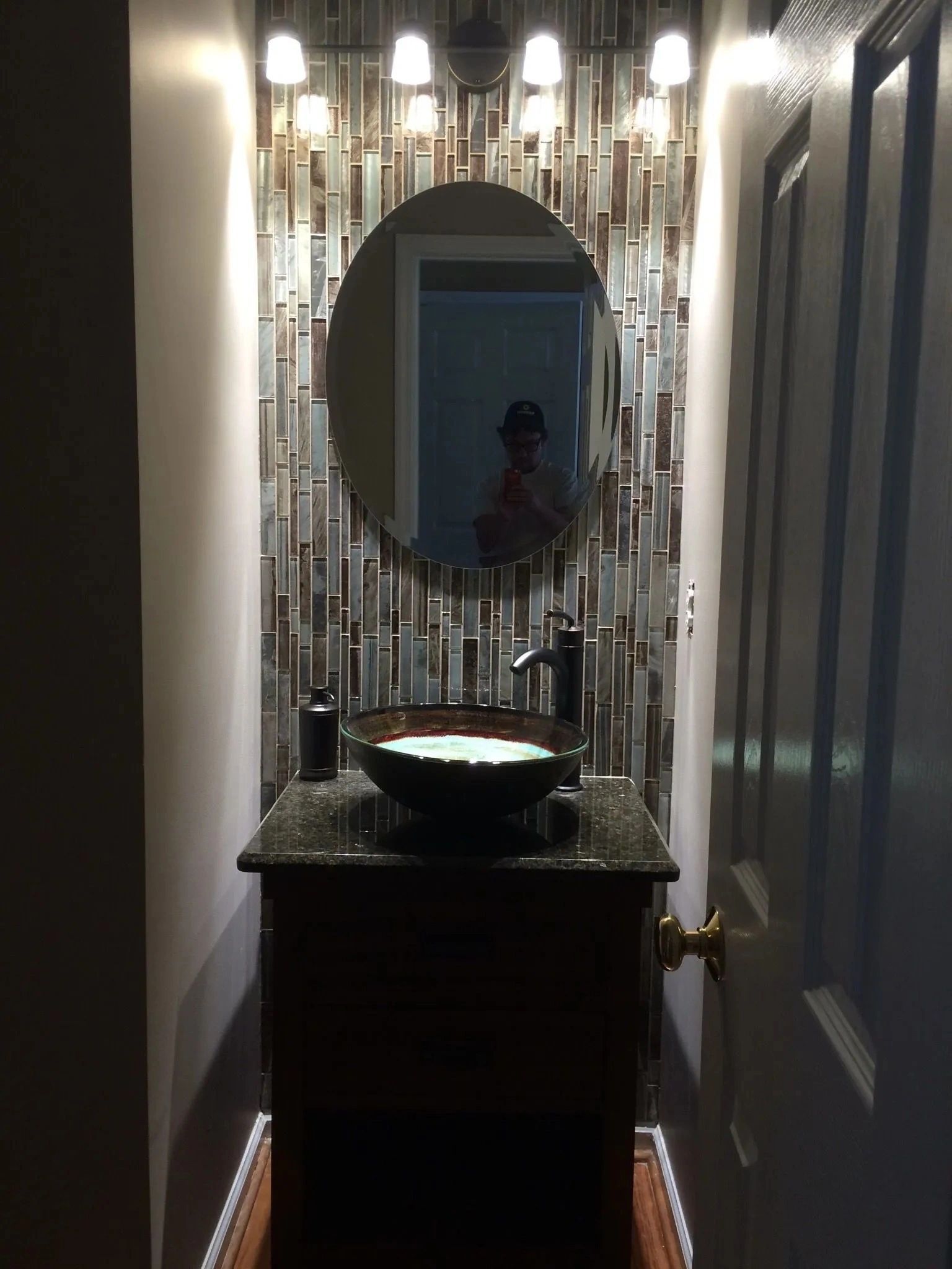Narrow hallway with a decorative mirror, lit wall sconces, and a dark sink cabinet below.
