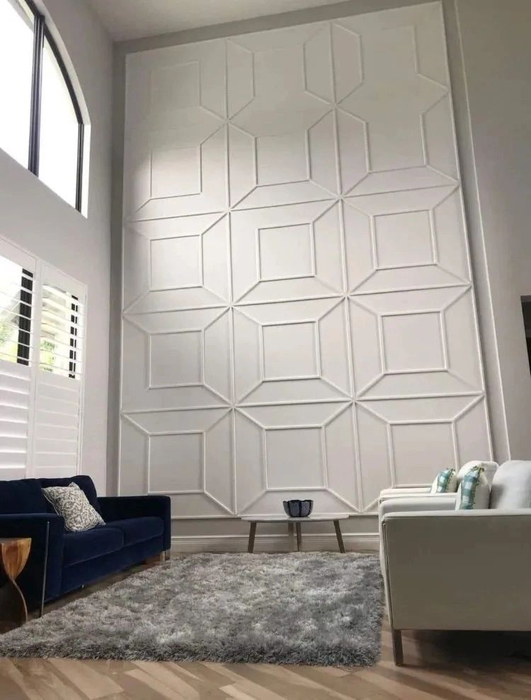 Modern living room with tall geometric accent wall, blue sofa, white chair, and gray rug.
