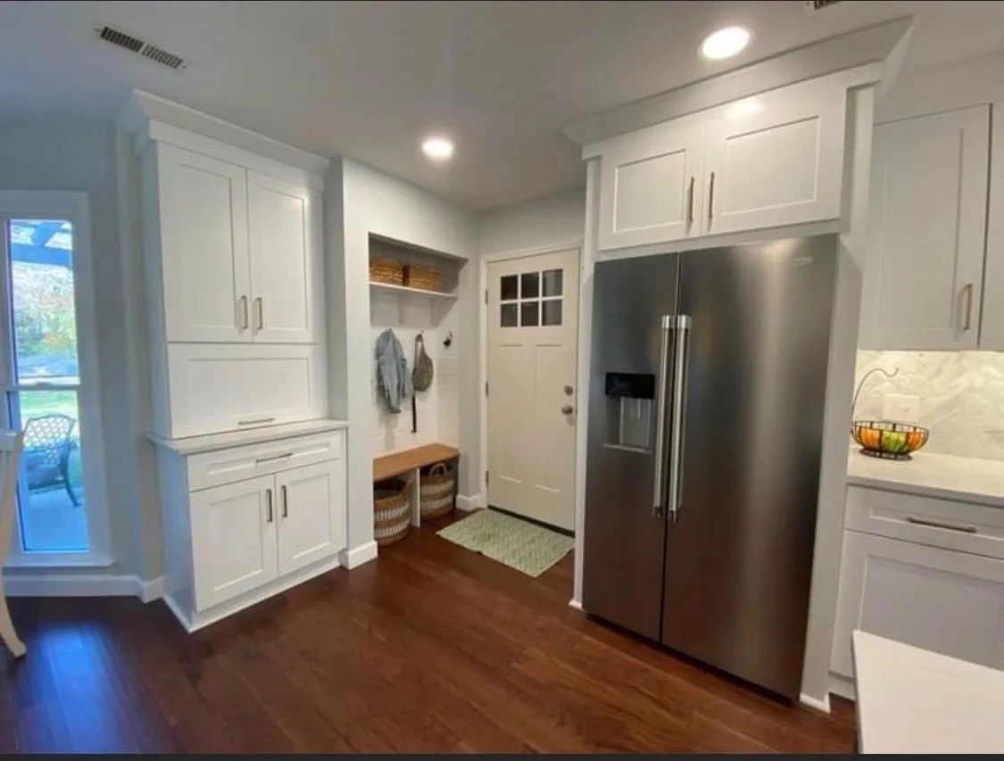 Bright white kitchen with stainless steel fridge, wood floors, and a small entry bench by the door
