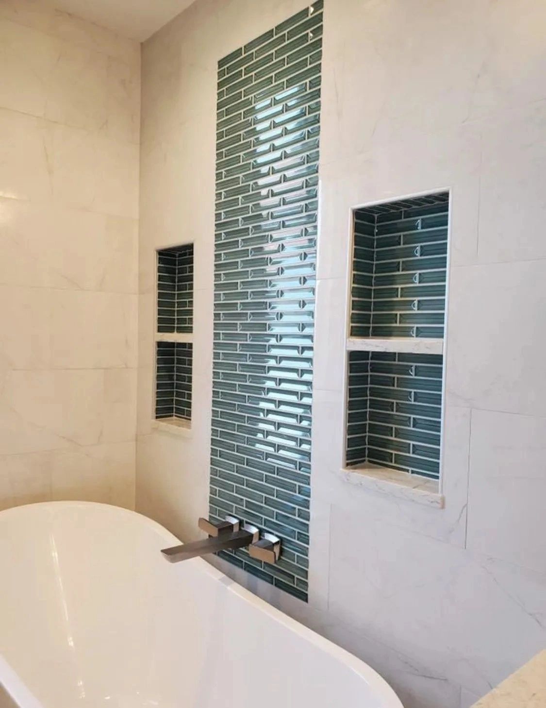 Bathroom tub and wall with blue mosaic-tile niches and a chrome faucet, viewed from the tub corner