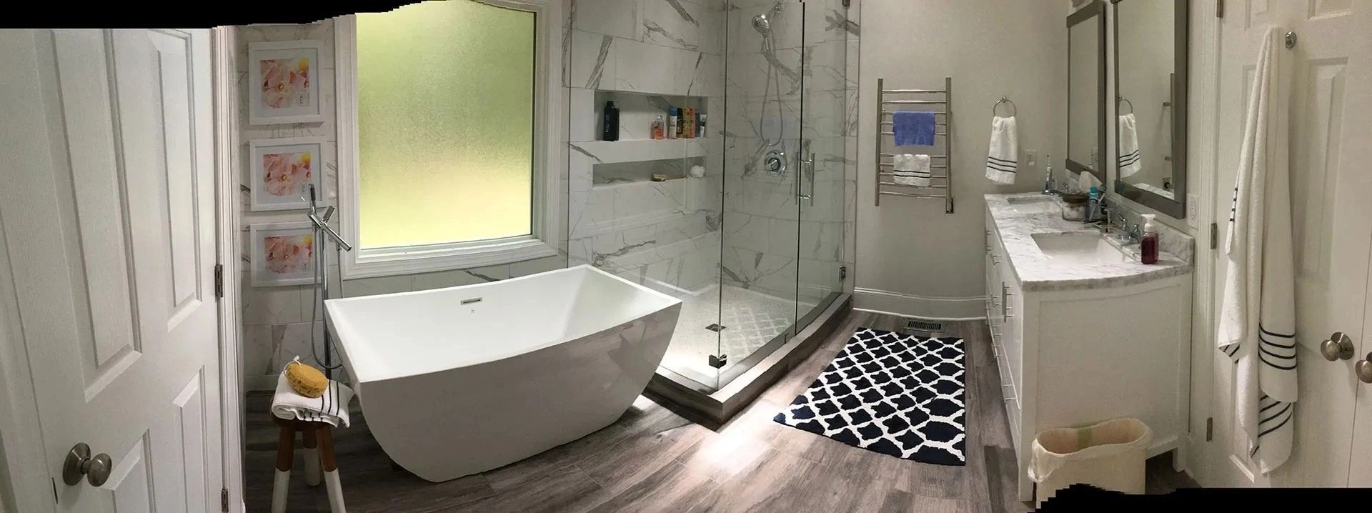 Bright modern bathroom with a freestanding tub, walk-in shower, sink vanity, and black-and-white rug.