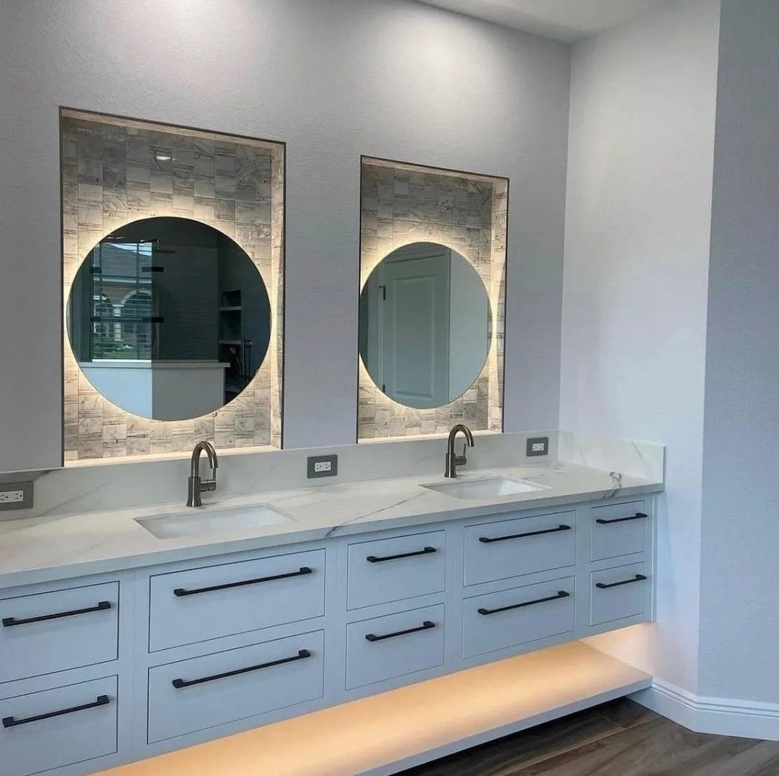 Modern double vanity with illuminated round mirrors and white cabinetry in a bright bathroom