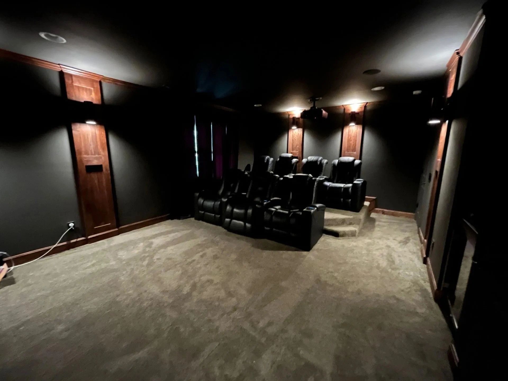 Dark home theater room with black recliners, wall sconces, and carpeted floor