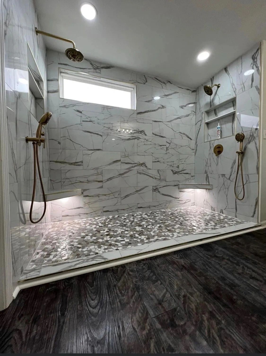 Modern shower with marble tile walls, rain showerheads, and pebble mosaic floor under recessed lights