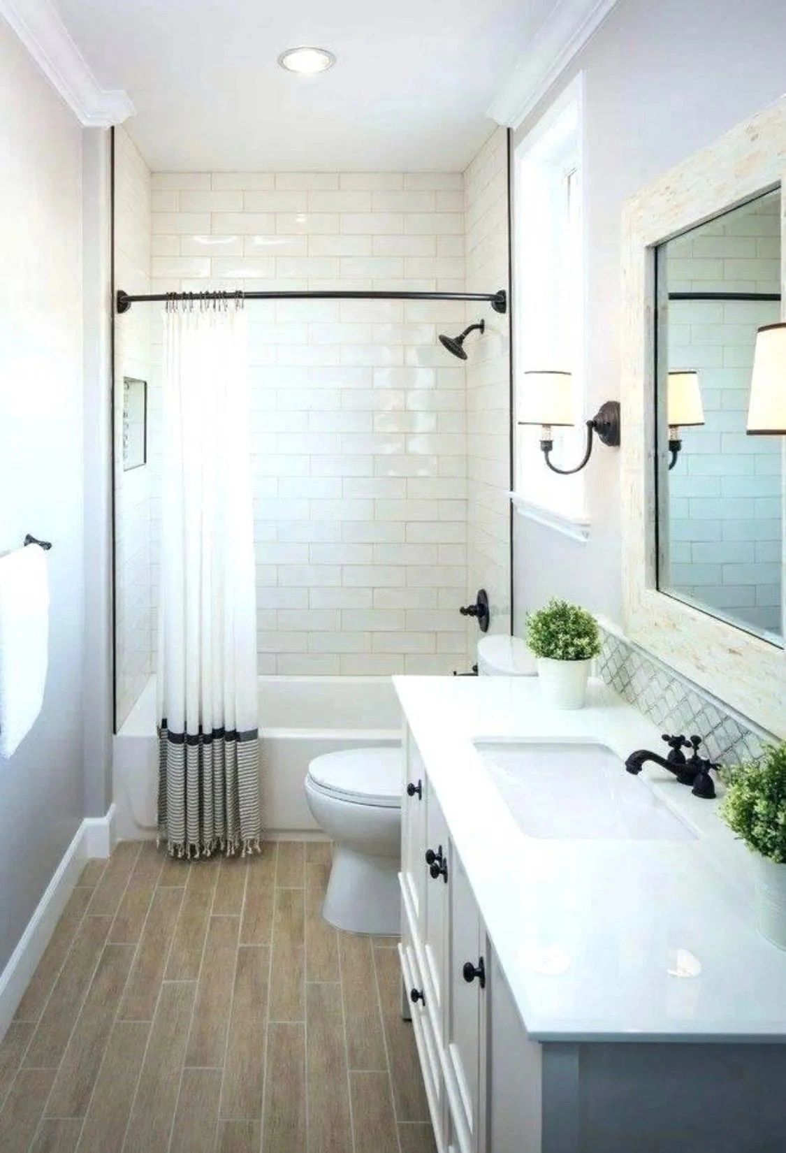 Bright white bathroom with walk-in shower, toilet, vanity sink, mirror, and wood-look floor tiles