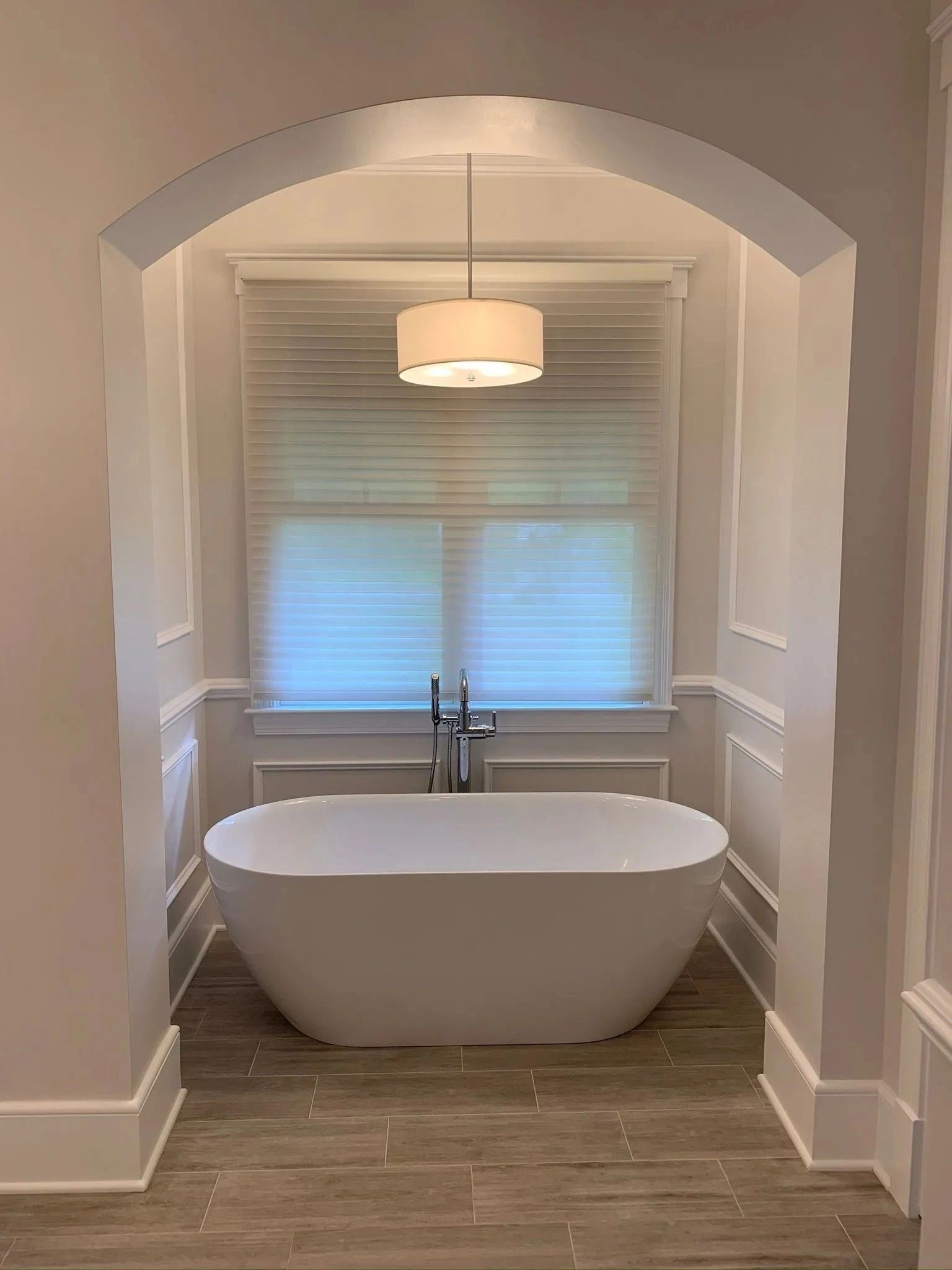 Elegant bathroom with a white freestanding tub beneath a pendant light and arched doorway.