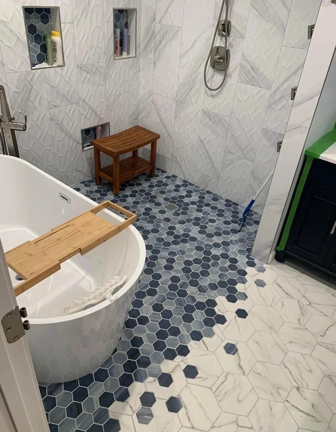 Small bathroom with a bathtub, hexagonal tile floor, wooden stool, and wall-mounted shower fixtures.