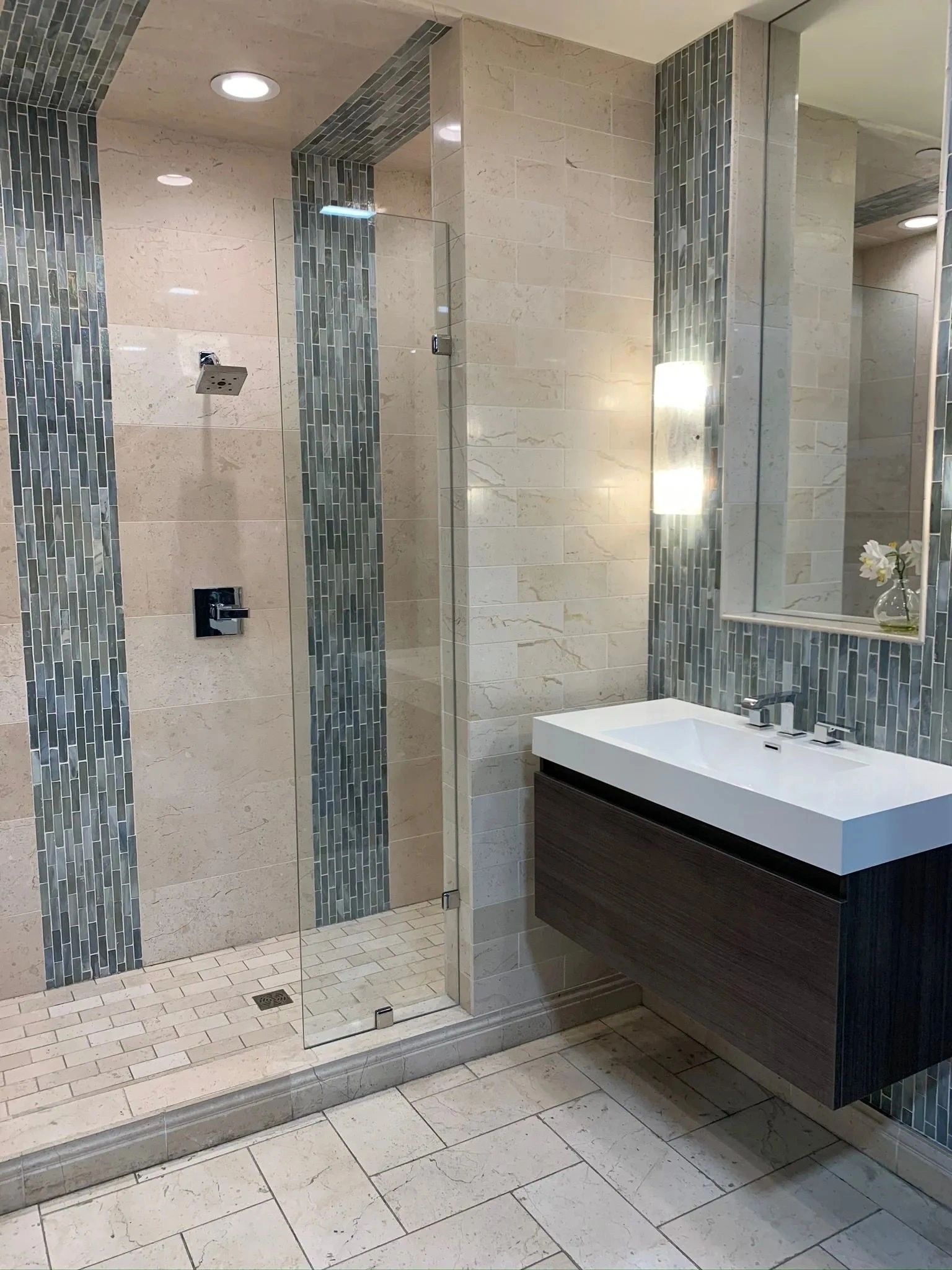 Modern bathroom with glass shower, beige tile, and wall-mounted sink vanity