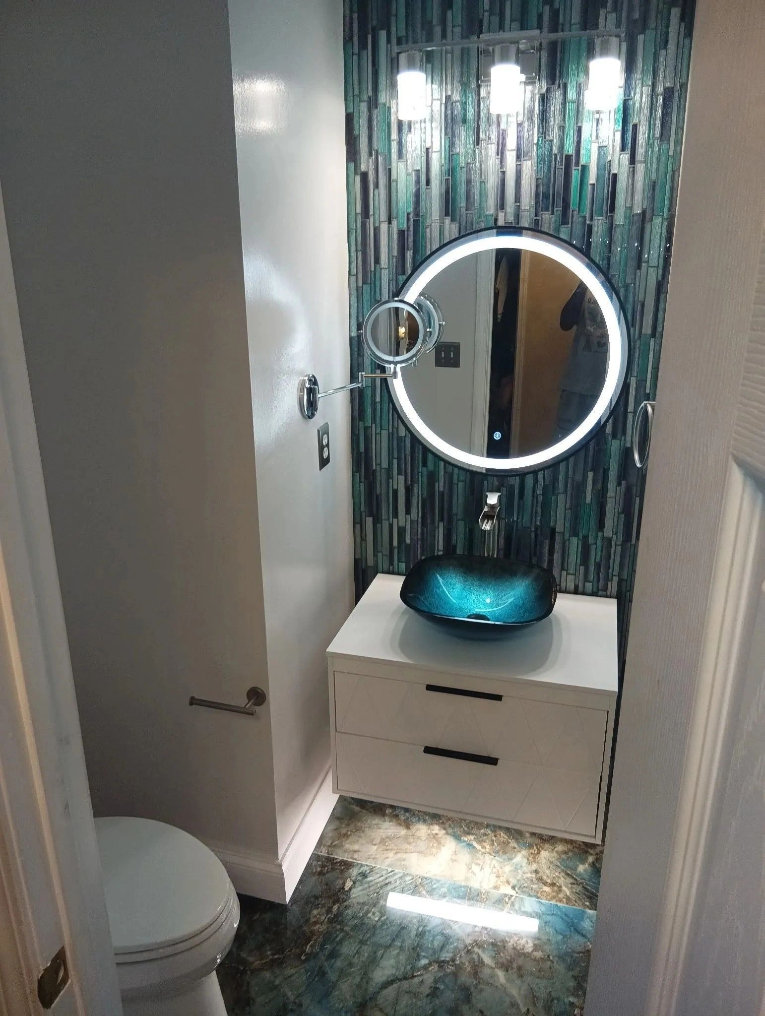Small bathroom vanity with round mirror, teal vessel sink, and mosaic shower curtain beside a toilet.