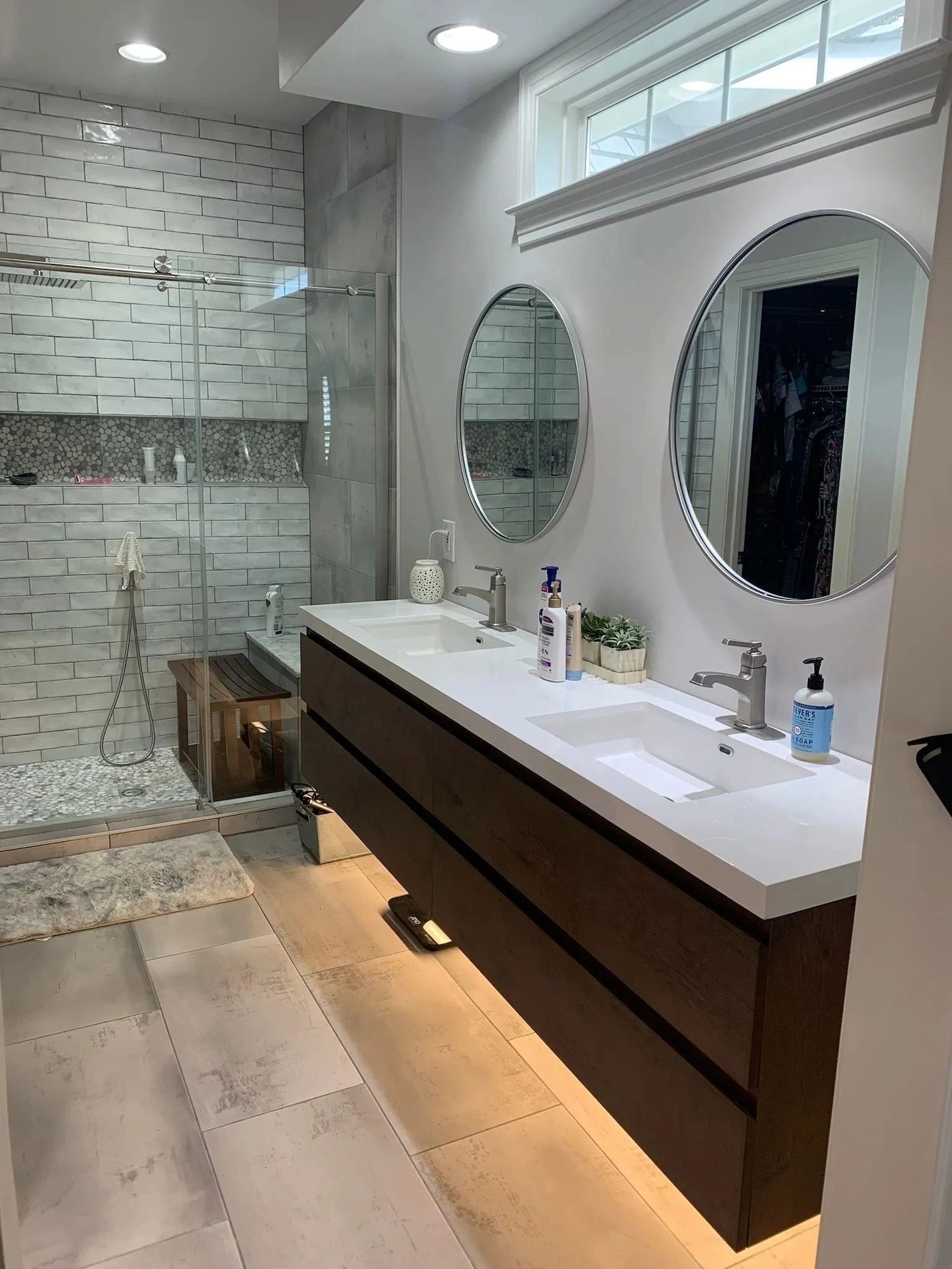 Modern bathroom with glass shower, double vanity, oval mirrors, and a tiled floor