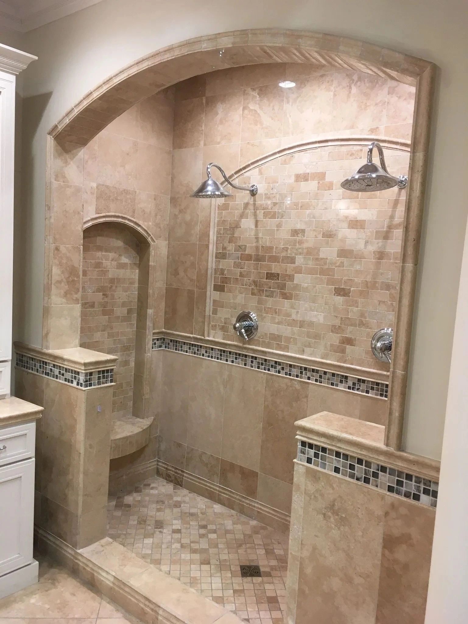 Stone-tiled walk-in shower with arched ceiling, decorative border, and dual showerheads